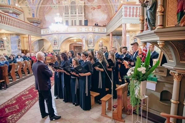 Chór z dyrygentem stoją i śpiewają w kościele