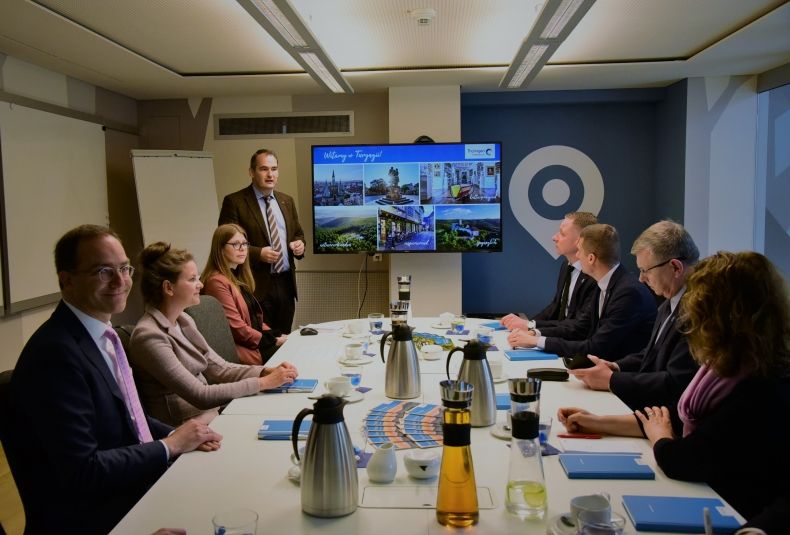 zdjęcie grupowe całej delegacji Polski i Turyngii, siedzą przy stole, wszyscy patrzą na prezentację wyświetloną na telewizorze