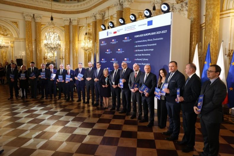 Wicemarszałek Łukasz Smółka stoi z pozostałymi uczestnikami wydarzenia w zabytkowej sali Zamku Królewskiego w Warszawie.
