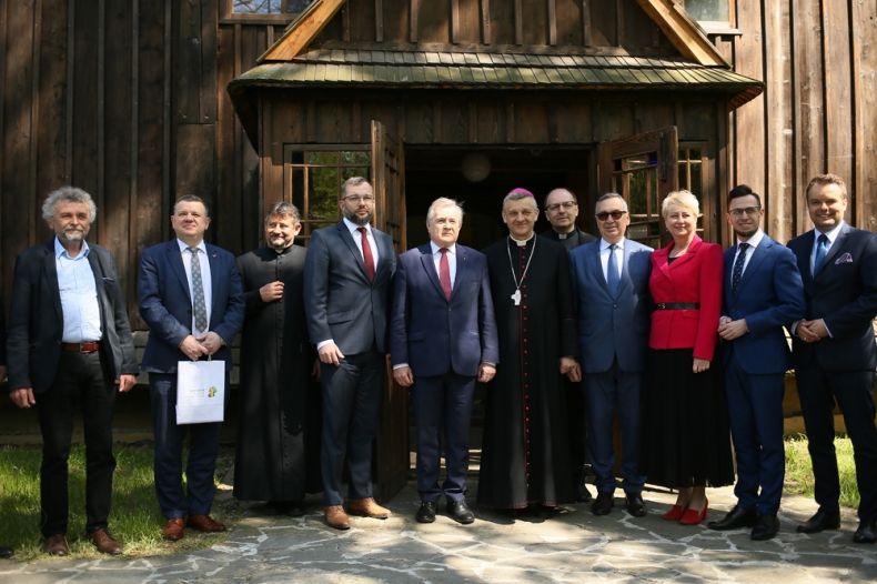 Premier Piotr Gliński, biskup prof. Roman Pindel, Iwona Gibas z zarządu województwa oraz m.in. posłowie przed zabytkowym drewnianym kościółkiem 