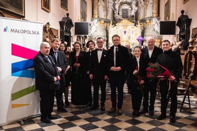 Radny województwa Mirosław Dróżdż stoi wewnątrz zabytkowego kościoła z muzykami.