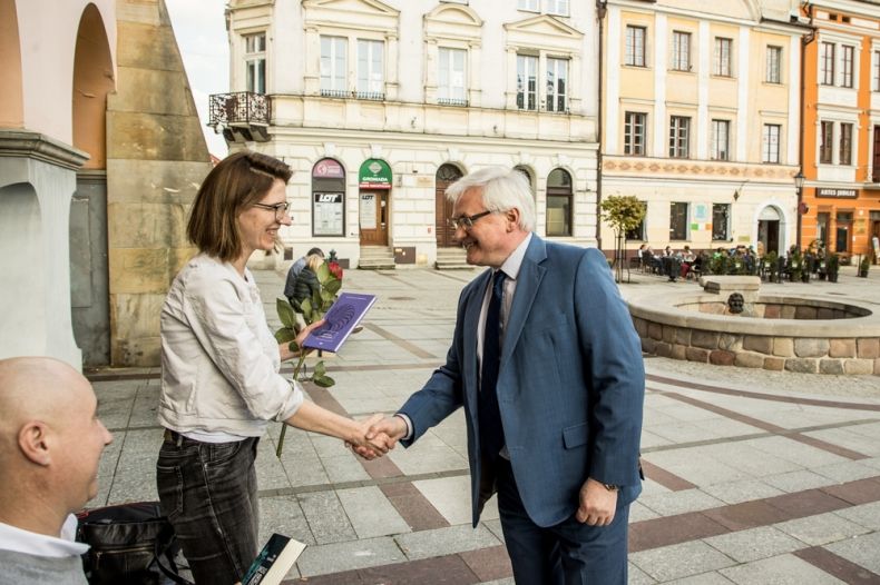 Wicemarszałek Józef Gawron podaje rękę kobiecie w białej bluzce, trzymającej książkę i czerwoną różę.