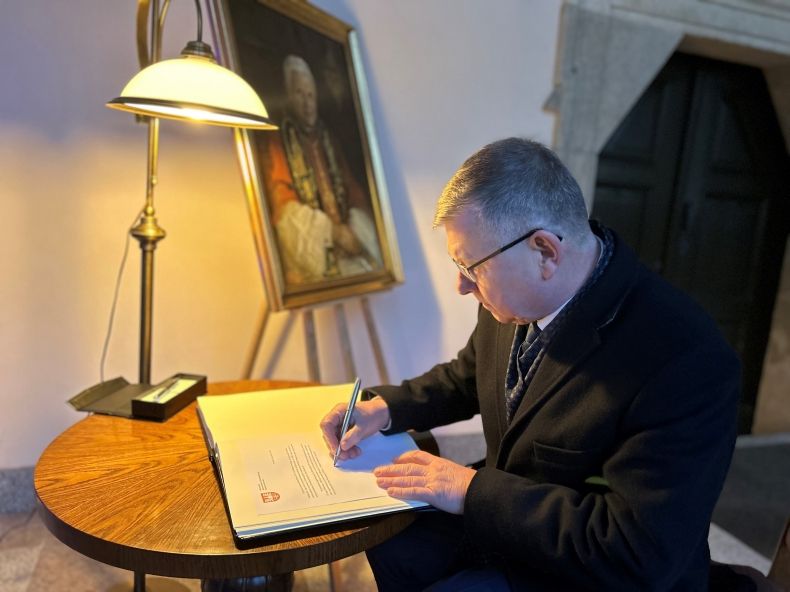  marszałek podczas wpisu do księgi kondolencyjnej; siedzi przy stoliku, na którym leży duża księga, obok pióro, lampka stojąca i obraz papieża