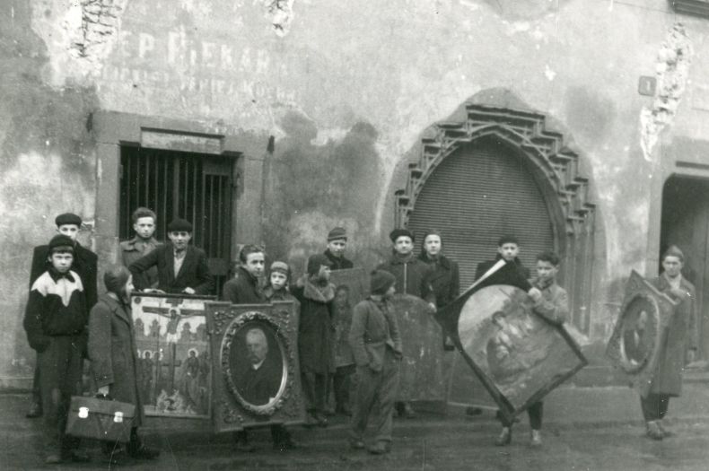 Grupa chłopców stojących przed budynkiem, trzymająca eksponaty muzealne/obrazy.