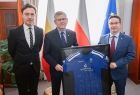 Dwaj mężczyźni oraz wicemarszałek Witold Kozłowski trzymający niebieską koszulkę w ramce.