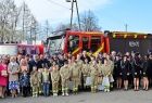 Uczestnicy uroczystości stoją na placu, w tle nowy samochód