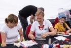 Kobieta w czerwonych koralach szyjąca materiałową laleczkę. 