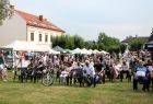 Ludzie siedzą na trawie, z tyłu widoczny budynek.