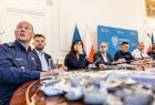 Policjant siedzi przy stole. Obok siedzą inni ludzie.