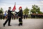 Strażaka przekazuje proporzec młodym strażakom.