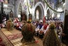 Wieńce dożynkowe stoją w kościele przy ołtarzu. W ławach siedzą ludzie.