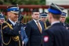 Wicemarszałek Łukasz Smółka stoi na placu. Przed nim stoi dwóch strażaków.