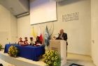 Wicemarszałek Ryszard Pagacz stoi na scenie przy mównicy. Obok przy stole siedzą władze uczelni.
