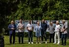 Uczestnicy wydarzenia stoją na trawie przed planszami.