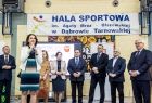 Uczestnicy wydarzenia stoją na hali sportowej.