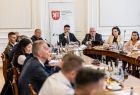 Marszałek Łukasz Smółka i wicemarszałek Ryszard Pagacz siedzą przy stole. Obok siedzą inni ludzi.,