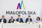 Marszałek Łukasz Smółka siedzi z ludźmi w sali obrad zarządu. Za nimi logo Małopolska.