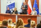 Wicemarszałek Ryszard Pagacz stoi przy stole. Obok siedzą inni ludzie.