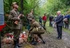 Wicemarszałek Ryszard Pagacz składa wieniec pod krzyżem w lesie. Obok żołnierze w historycznych strojach.