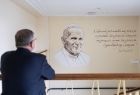 Wicemarszałek Witold Kozłowski patrzący na mural z wizerunkiem i cytatem św. Jana Pawła II.