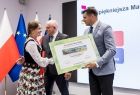 Marszałek Łukasz Smółka wręcza nagrodę kobiecie w stroju ludowym.