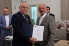 Wicemarszałek Ryszard Gawron stoi z mężczyzną i dokumentem. Z tyłu inni ludzie.