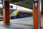Żółto-niebieski pociąg z grafiką Funduszy Europejskich stojący na peronie.