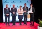 Kapłan w jasnej koszuli na scenie z przedstawicielami Sejmiku.