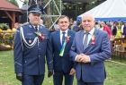Wicemarszałek Ryszard Pagacz stoi na trawniku razem z policjantem i mężczyzną w garniturze.