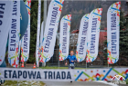 Biegacz na trasie zawodów pomiędzy licznymi reklamami Etapowej Triady 