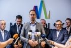 Prezydent Tarnowa Jakub Kwaśny stoi przed mikrofonami. Za nim widoczni inni ludzie.