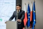Marszałek Łukasz Smółka stoi przy mównicy. Za nim widoczne flagi.