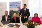 Wicemarszałek Łukasz Smółka stoi przy stole. Obok siedzą ludzie.