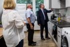 Wicemarszałek Witold Kozłowski otwiera szafkę w kuchni. Obok stoi kobieta i mężczyzna, widoczna też pralka.