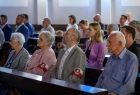 Osoby siedzące w ławce z patriotycznymi opaskami na ramionach.