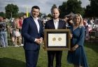 Marszałek Łukasz Smółka. Obok mężczyzna trzymający złoty medal i kobieta w zielonej sukience.
