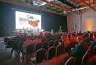 Hala expo, na pierwszym planie siedzą ludzie.