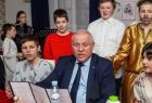 Wicemarszałek Ryszard Pagacz siedzi przy stole. Obok stoją dzieci.