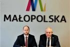 Wicemarszałek Ryszard Pagacz siedzi przy stole. Obok siedzi mężczyzna. Za nimi na ścianie widoczne logo Małopolska.