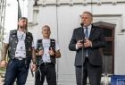 Wicemarszałek Ryszard Pagacz stoi przy mikrofonie. Obok dwóch motocyklistów.
