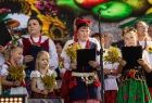Dzieci w strojach krakowskich stoją na scenie podczas występu.