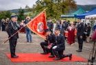 Strażacy klęczą na czerwonym dywanie przed sztandarem.