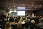 Sala konferencyjna. Na pierwszym planie siedzą ludzie.