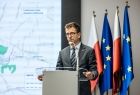 Burmistrz Radosław Kuś stoi przy mównicy. Za nim widoczne flagi.
