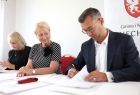 Dokument podpisuje burmistrz miasta i gminy Miechów Dariusz Marczewski. Obok burmistrza za stołem prezydialnym siedzi Iwona Gibas z zarządu województwa