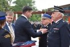 Wicemarszałek Łukasz Smółka przypina medal strażakowi. Obok stoi radny województwa Mirosław Dróźdż.