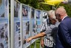 Jan Więcek pokazuje palcem zdjęcia na wystawie. Obok stoi wicemarszałek Ryszard Pagacz.