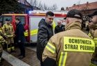 Wicemarszałek Łukasz Smółka podaje rękę strażakowi OSP. Z tyłu widoczny wóz strażacki.