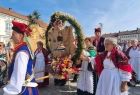 Ludzie w strojach regionalnych niosą wieńce dożynkowe.