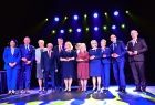Uczestnicy wydarzenia stoją na scenie. Za nimi widoczne światła.